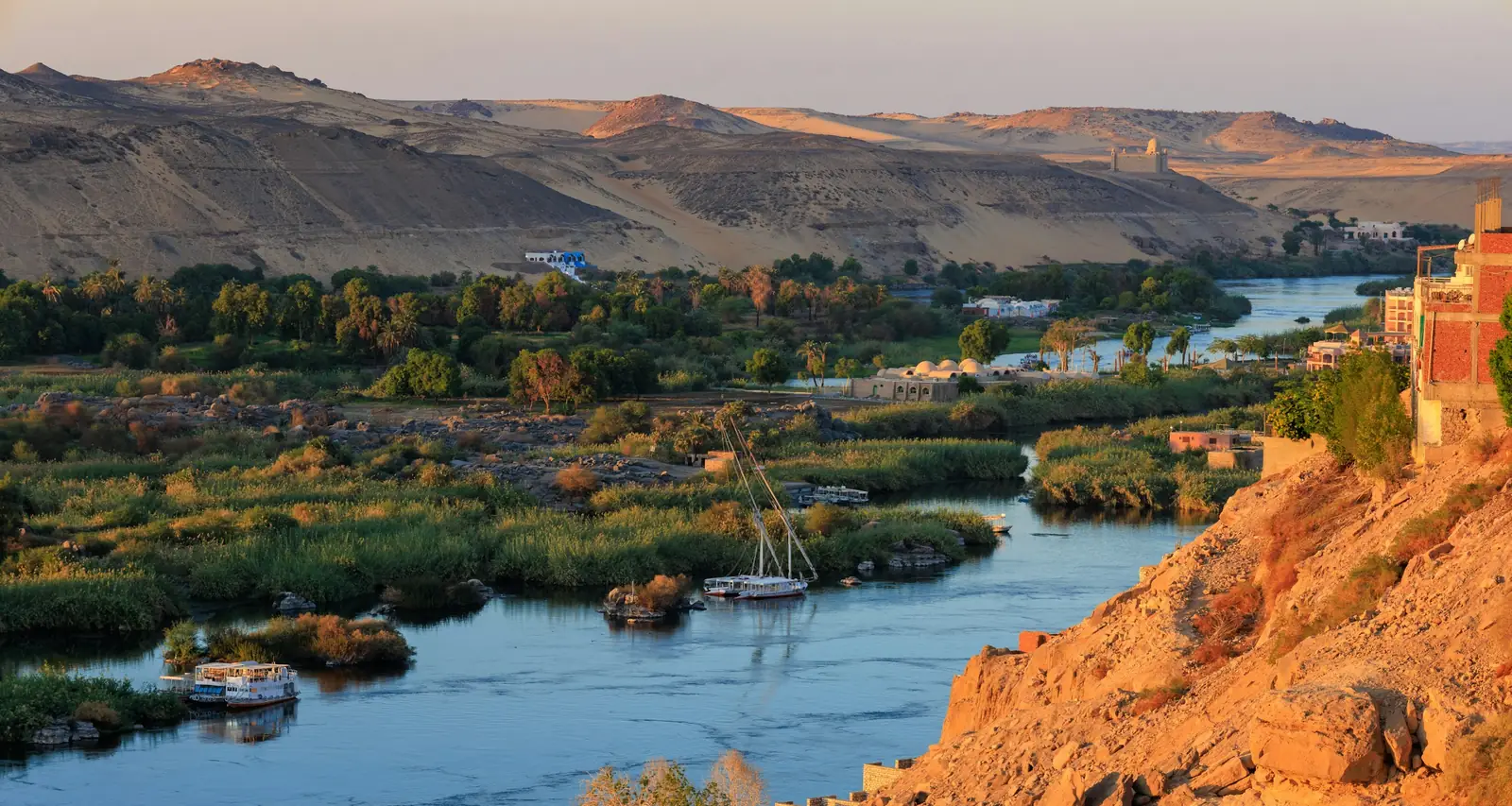 The Nile at Aswan in soft evening light, with sand dunes and green islands along the river
